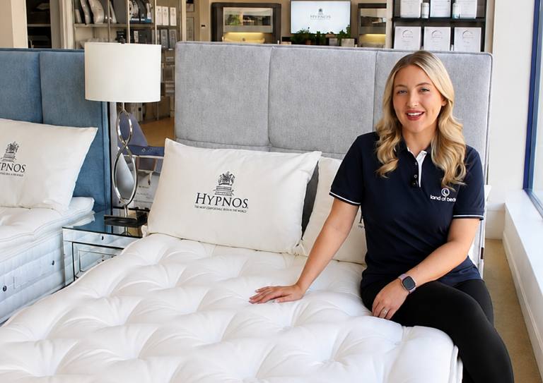 Charlotte Blythe sitting on a Hypnos mattress in a Land of Beds showroom, presenting one of our product videos.