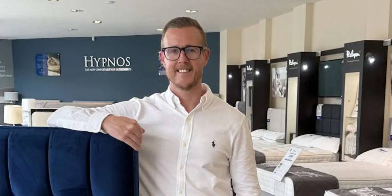 Mike Murray, Managing Director of Land of Beds, leaning on a headboard in a Land of Beds showroom.